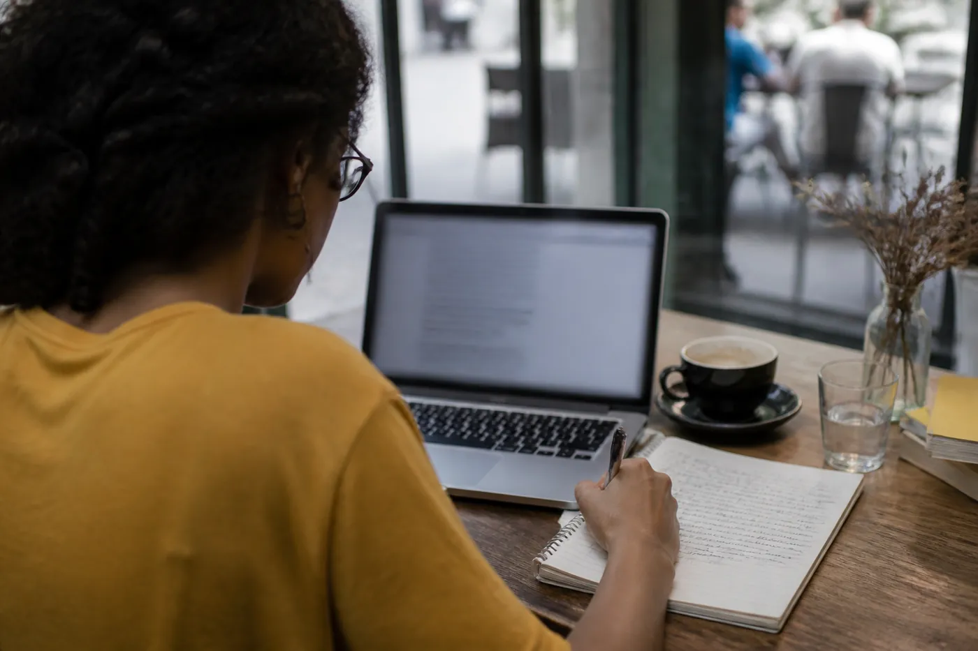 Pessoa pesquisando reclamações e anotações em um café, com a tela do notebook desfocada